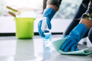 Husband housekeeping and cleaning concept, Happy young man in blue rubber gloves wiping dust using a spray and a duster while cleaning on floor at home.